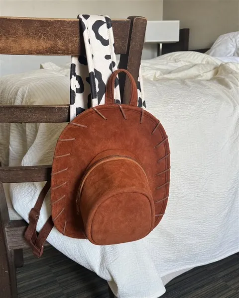 Brown cowboy hat backpack hanging from a wooden chair in a hotel room
