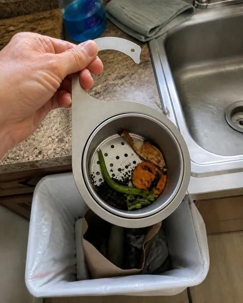 Customer lifting the removable basket to empty drained kitchen scraps into a trash bin