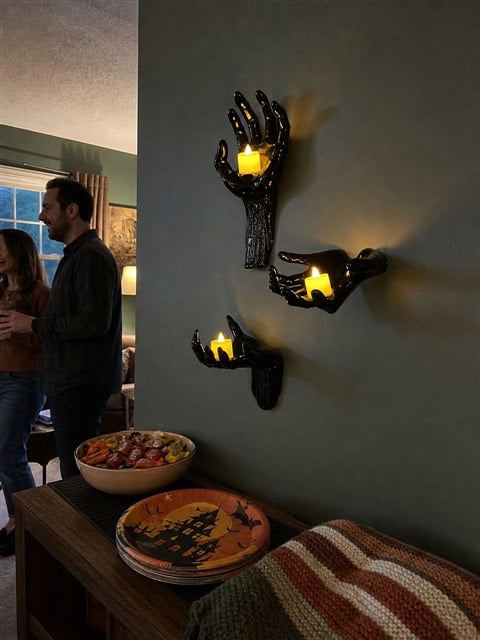 Three glowing black hand candle holders beside a Halloween snack table