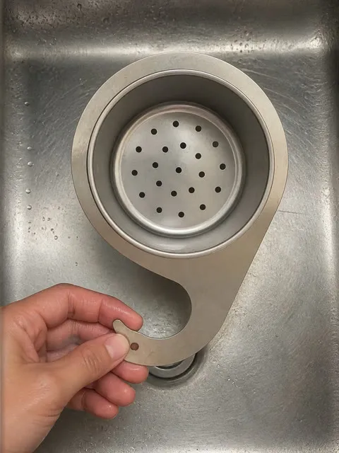 Customer holding the removable stainless basket and separate swan-hook support in a sink