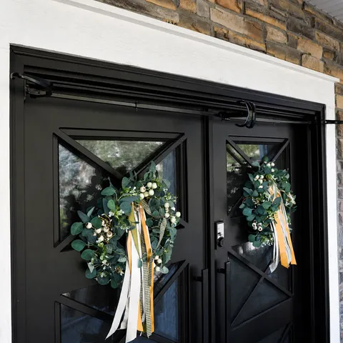 Black adjustable hanger spanning dark double doors with two green wreaths