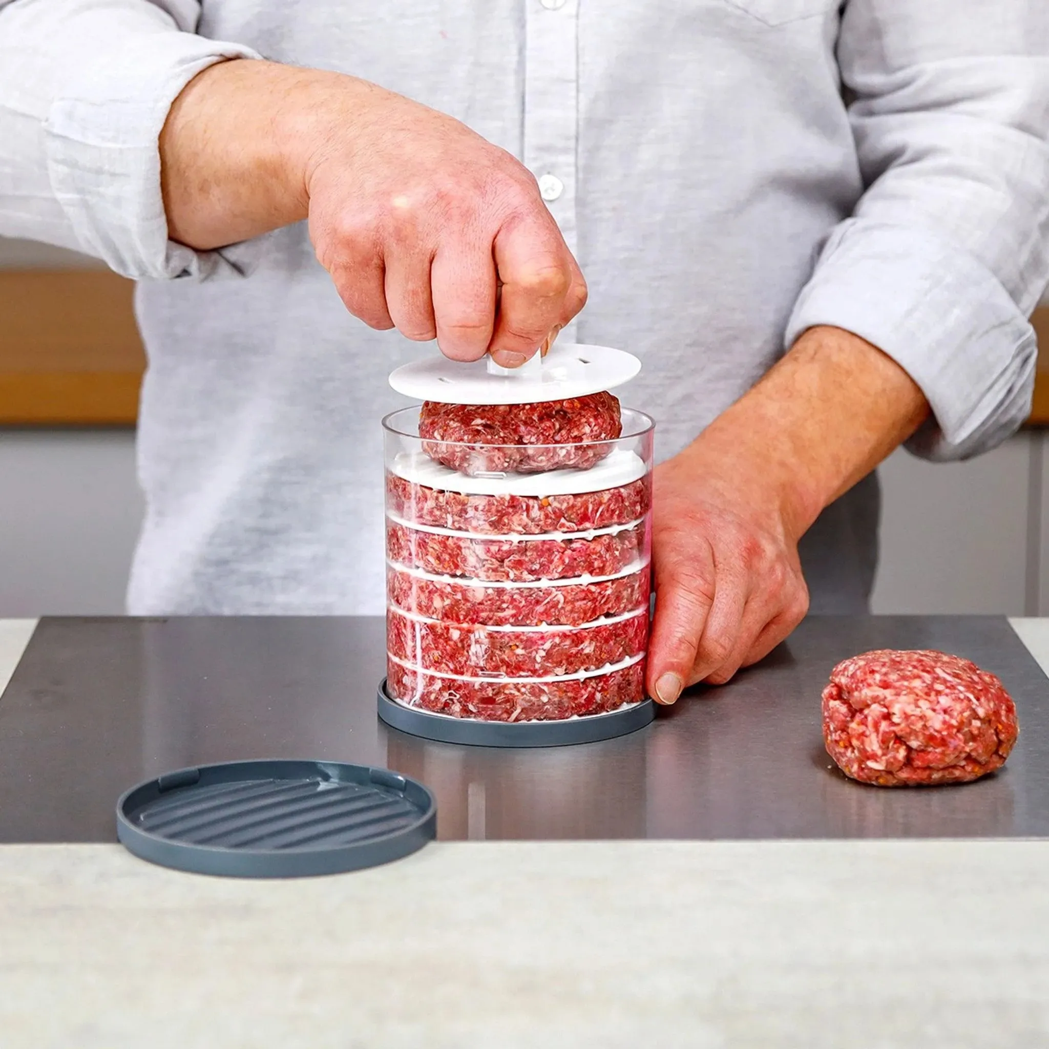 Cook pressing another round patty into a clear stacking container