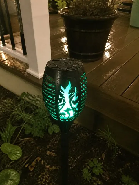 Green solar torch glowing beside a wet deck