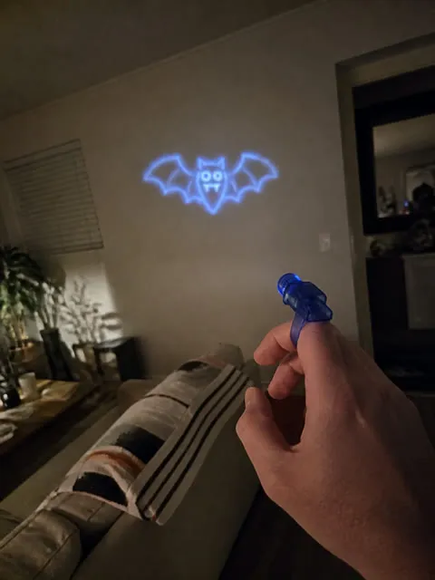Blue finger projector casting a bat shape in a living room