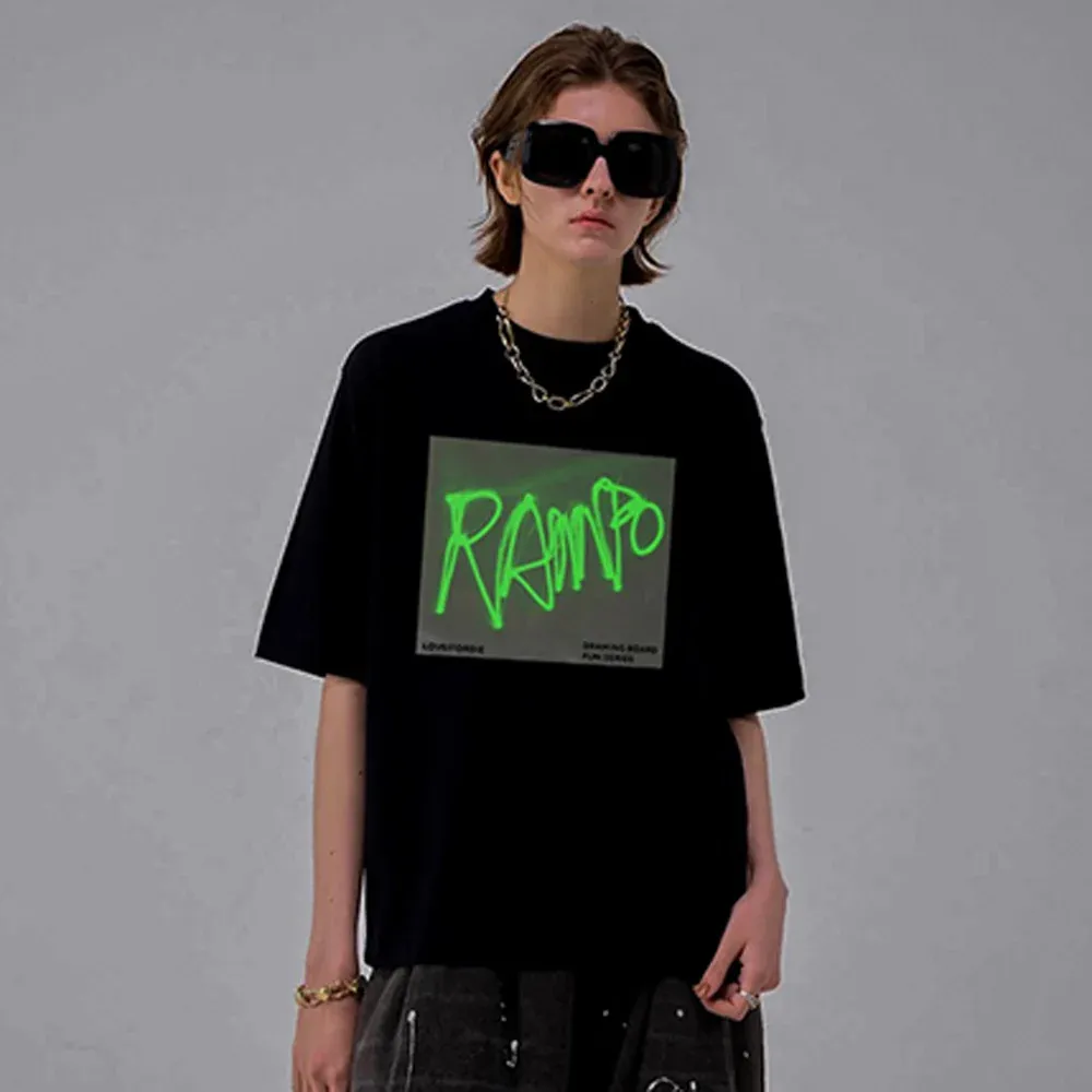 Black glow-in-the-dark drawing T-shirt worn by a model, with a bright green glowing design on the front panel