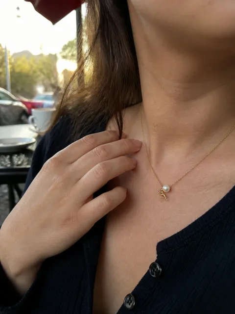 Gold-tone pearl pusher necklace worn at an outdoor cafe