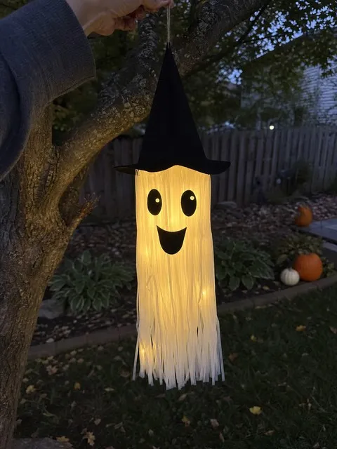 Black hat light-up tassel ghost hanging from a backyard tree