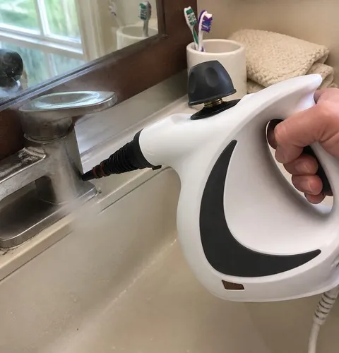 Handheld steam cleaner aimed at a bathroom faucet edge