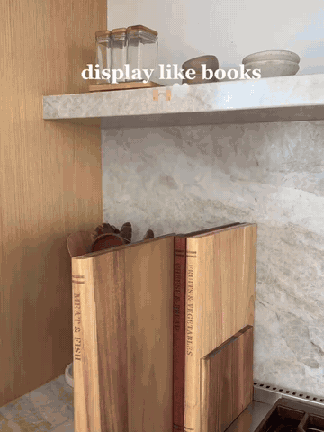 Three book-style solid wood cutting boards being selected from their upright stand