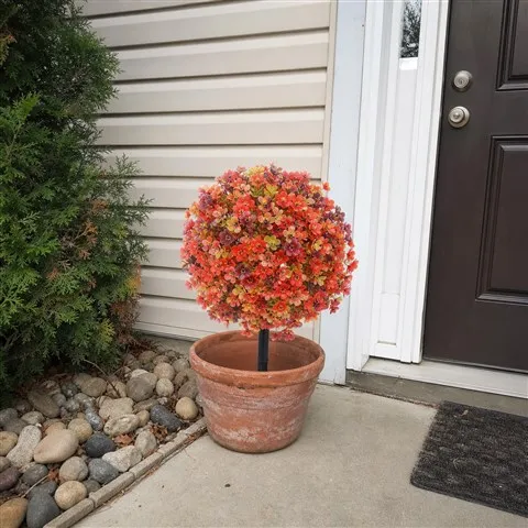Artificial fall flower topiary in a terracotta planter by a front door