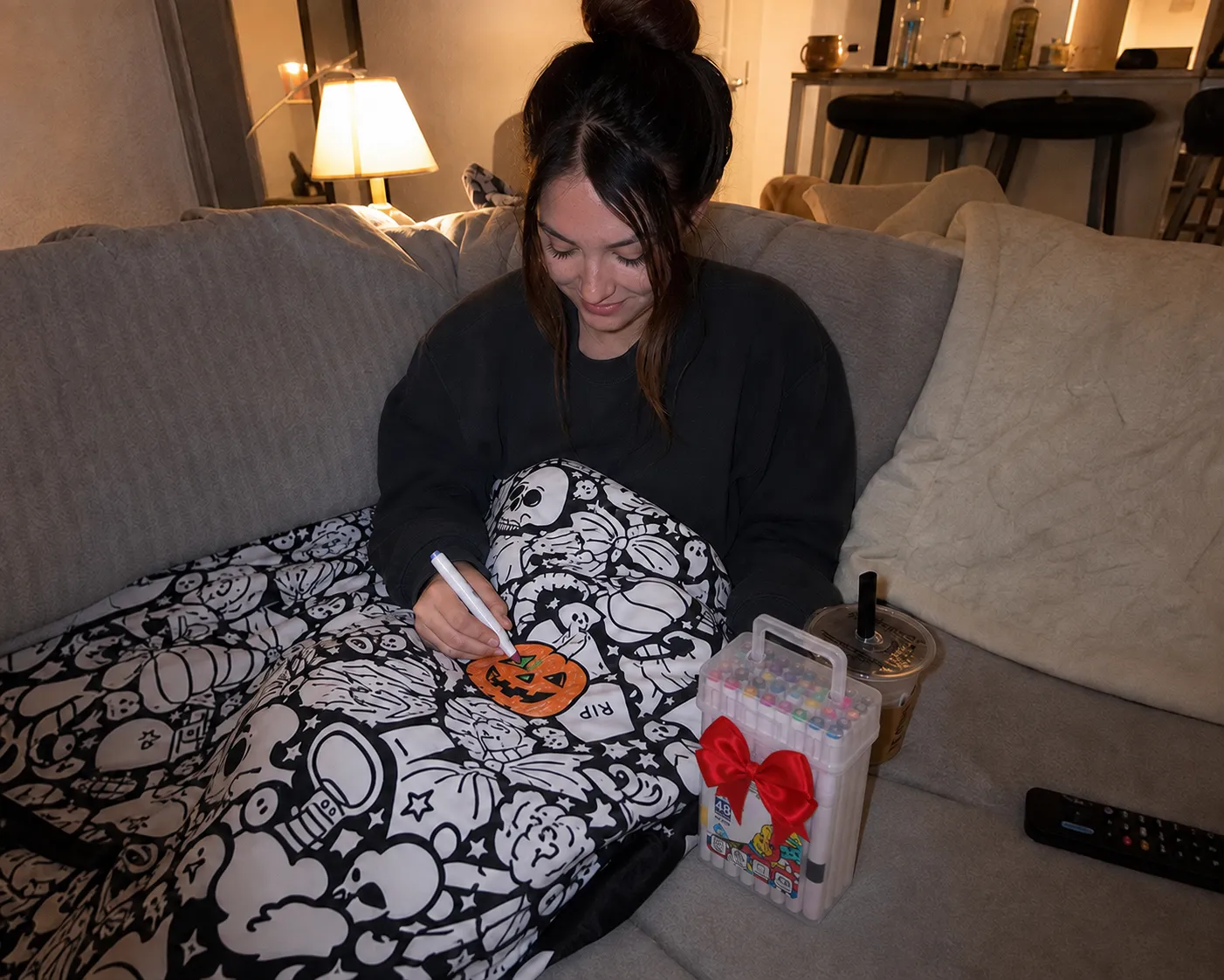 Young adult coloring the Halloween blanket on a sofa