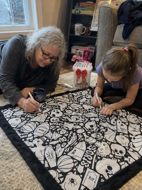 Grandmother and child coloring a Halloween blanket at home
