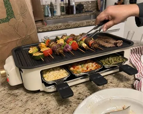 Tabletop grill cooking skewers and individual sides in an apartment kitchen
