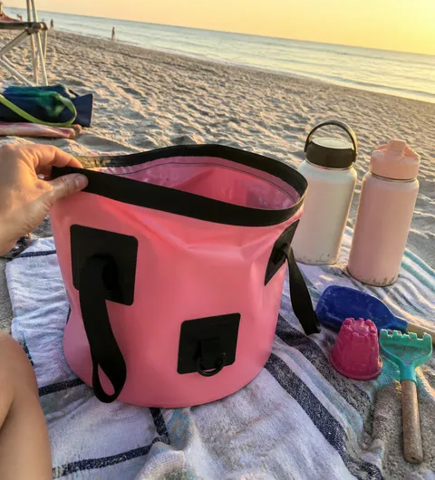 Pink collapsible bucket being folded on a beach towel