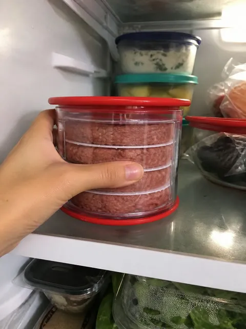 Stacked hamburger patties stored in a clear container on a refrigerator shelf